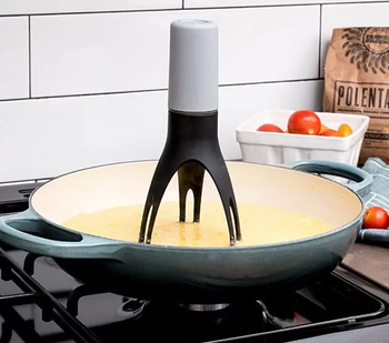 A stirrer is shown in a pan with a yellow mixture on the stove. A container of tomatoes and a bag of polenta are in the background.