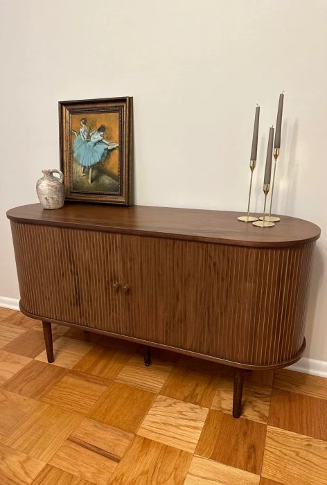 A sideboard adorned with a framed ballet artwork, a ceramic vase, and three sleek candleholders, perfect for elevating home décor.