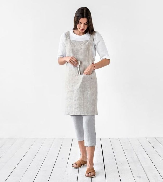 Model wearing the gray apron and tucking a wooden spoon into the pocket