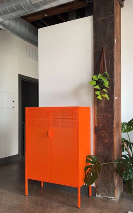 An orange cabinet with plants placed beside and on top, set in a modern industrial-style room with exposed ductwork.