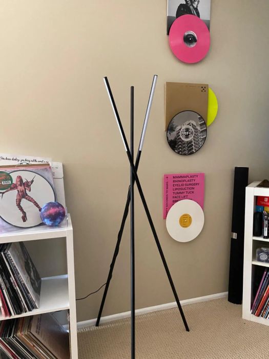 A contemporary black floor lamp stands in a room decorated with vinyl records on the wall and shelves filled with more records.