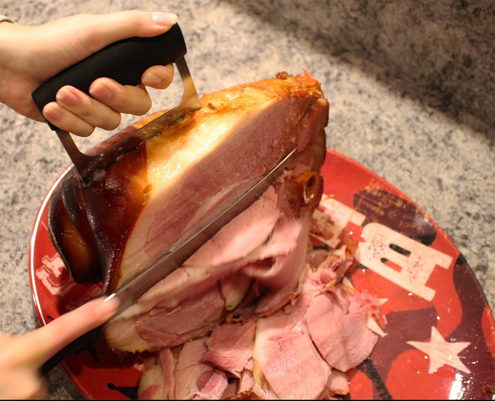 A person using one bear claw to hold a piece of turkey steady while slicing it with the other hand