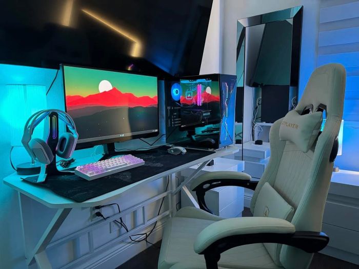 A gaming setup featuring a large monitor displaying a scenic mountain view, gaming PC with LED lighting, a white gaming chair, a headset, and a multicolored keyboard.