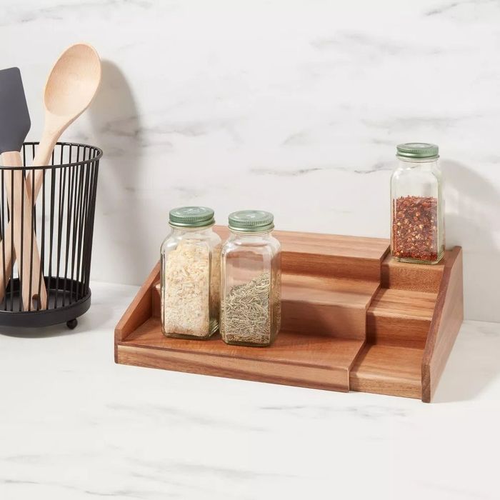 A three-tier expandable spice rack holding a variety of spices on a kitchen counter.