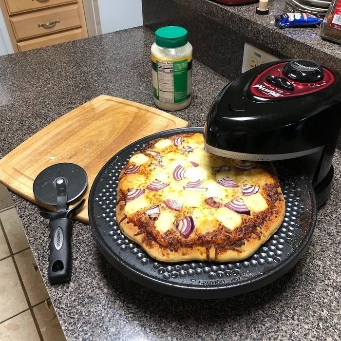A homemade pizza with various toppings baking inside the rotating pizza oven