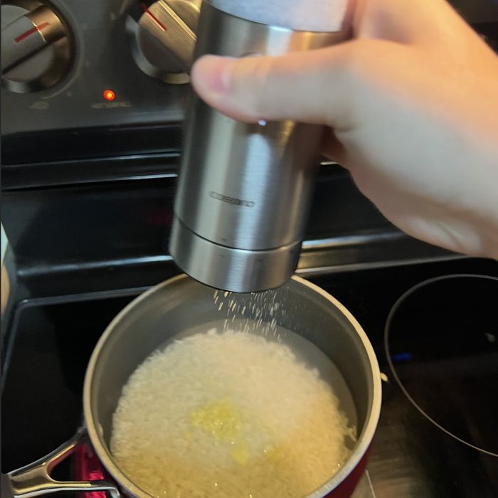 Person using a pepper grinder to season rice cooking on a stovetop