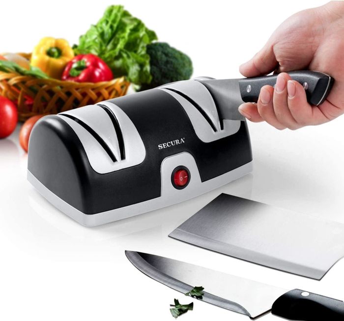 An electric knife sharpener with a hand sharpening a knife, surrounded by fresh vegetables, emphasizing its kitchen utility
