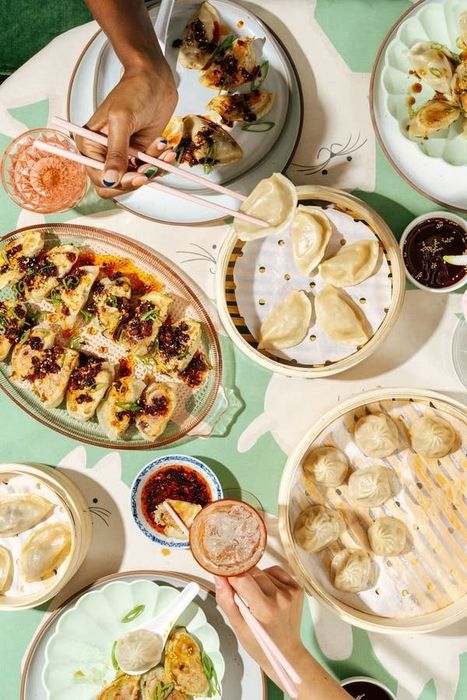 A bird’s-eye view of a table filled with various dumplings, dipping sauces, and drinks, with hands reaching in to enjoy the vibrant communal dining experience