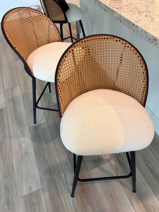 Two elegant barstools with curved, woven rattan backs and cream-colored cushioned seats, placed beside a countertop.