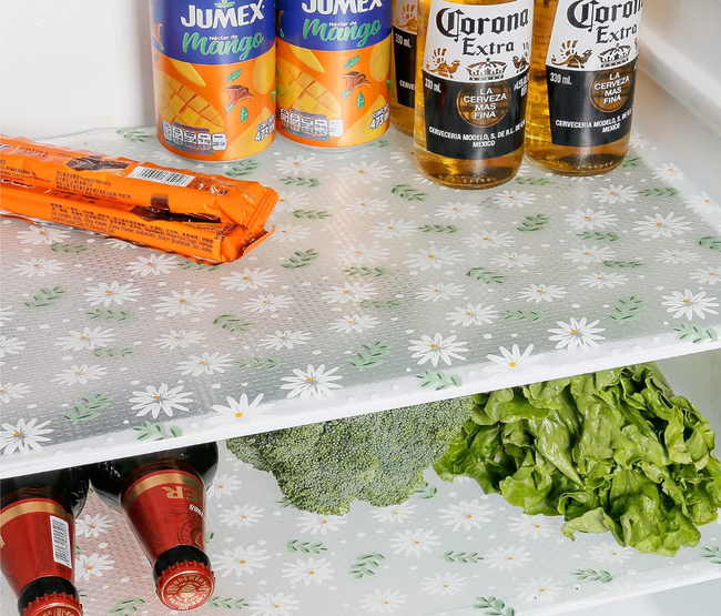 Fridge shelves covered with a clear liner featuring a white and green leaf and daisy print.