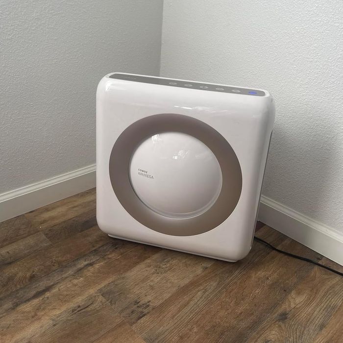 A sleek Airmega air purifier placed in the corner of a kitchen with wooden floors