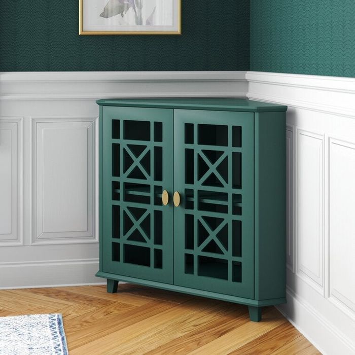 a teal corner cabinet featuring intricate door cutouts, placed in the corner of a room