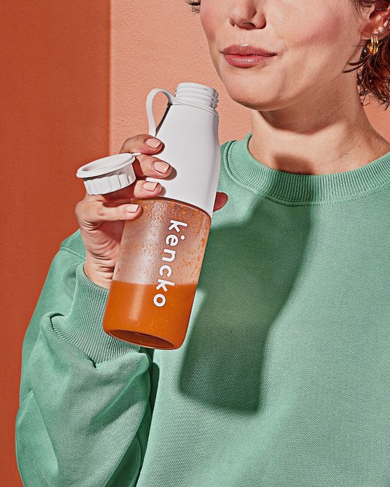 A person holding a Kencko smoothie bottle while dressed in a casual green sweatshirt