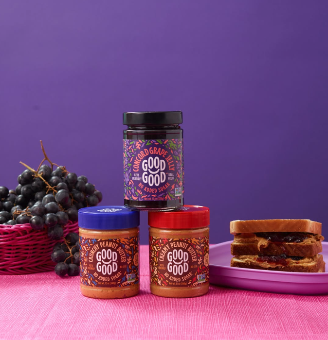 A variety of sugar-free grape and peanut butter spreads are neatly arranged alongside a basket of fresh grapes and a peanut butter and jelly sandwich on a plate