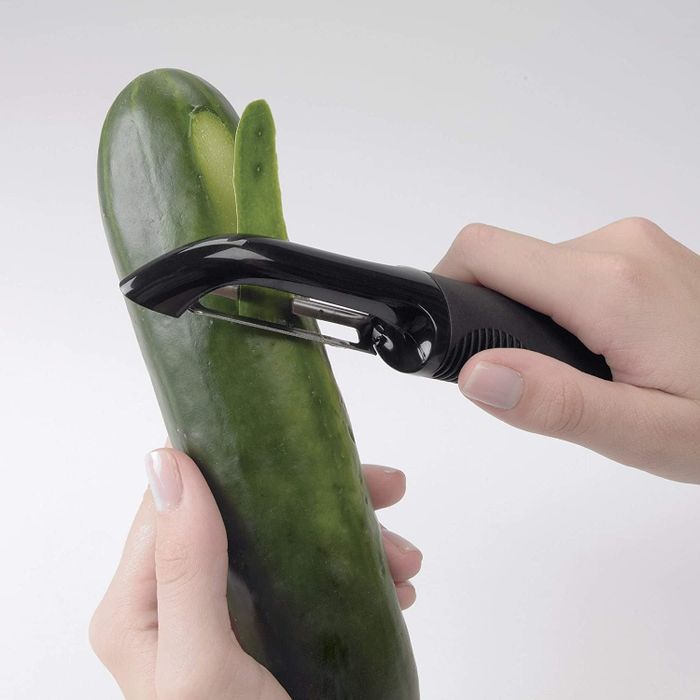 Hands holding a black peeler and peeling the side of a zucchini