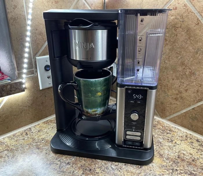 A Ninja coffee maker sits on the countertop as a green mug is filled with coffee.