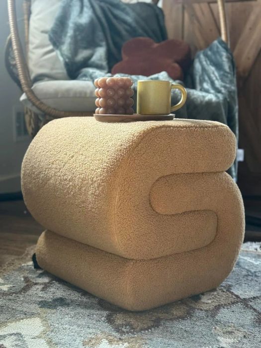 An oversized plush letter-shaped stool with a mug placed on top, set in a cozy home environment.
