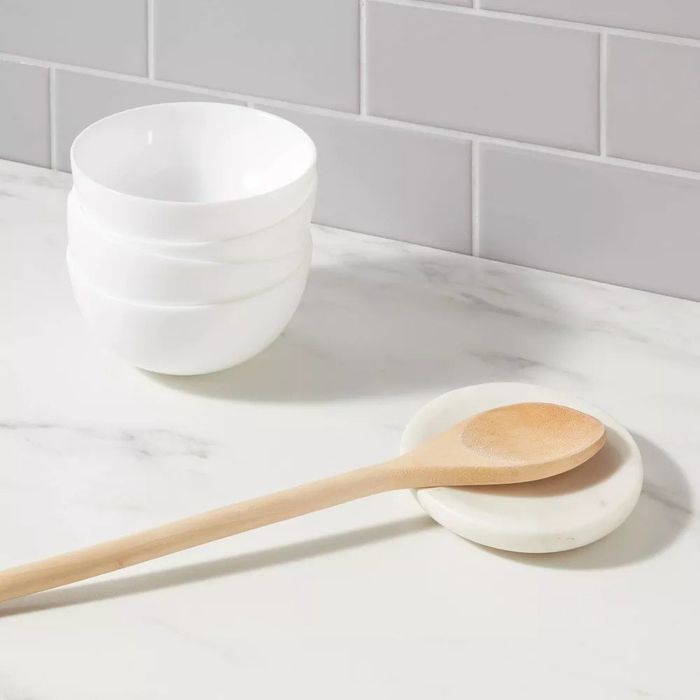 A wooden spoon resting on a circular marble spoon rest.