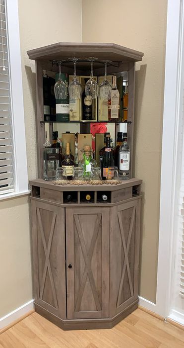 A brown wooden corner cabinet with glass panels, showcasing alcohol bottles and glasses inside