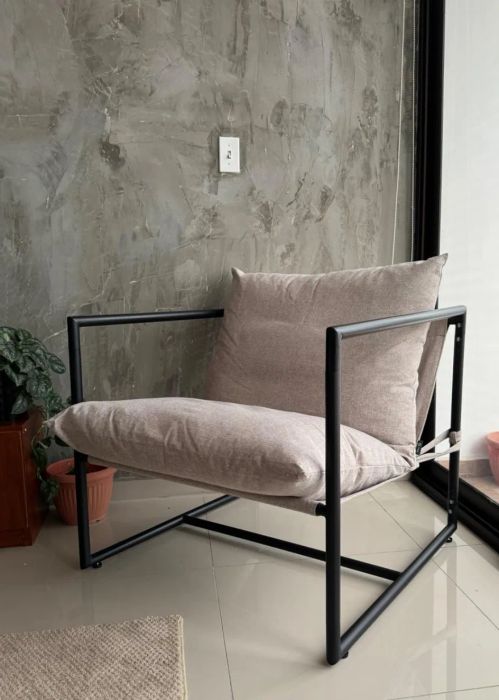 A sleek minimalist armchair with a metal frame and a soft cushion, placed by a glass sliding door with lush potted plants surrounding it.