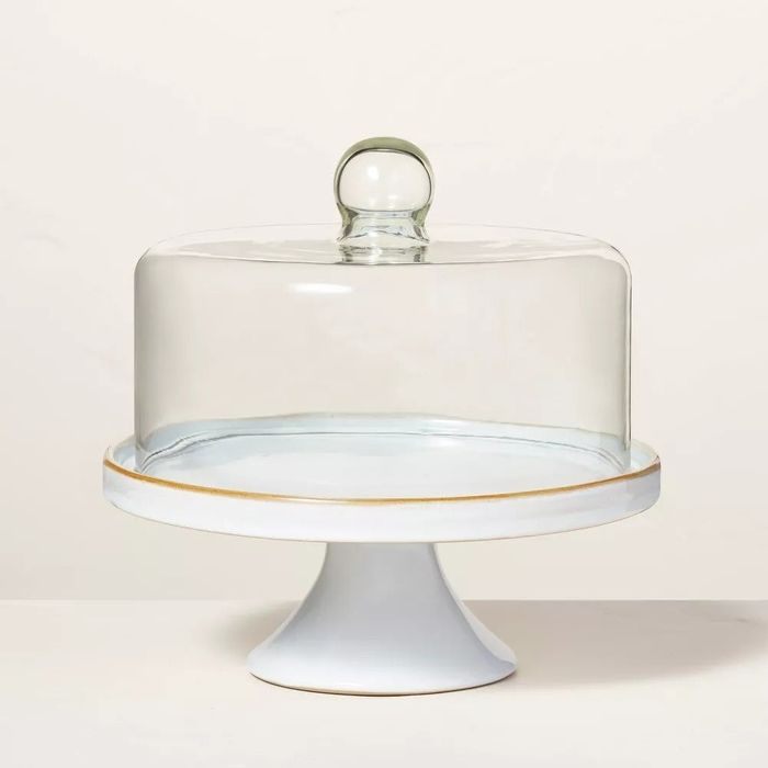 A glass cake dome resting atop a white pedestal stand.