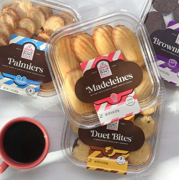 A selection of baked goods from Sugar Bowl Bakery, including Palmiers, Madeleines, Duet Bites, and Brownies, served alongside a cup of coffee