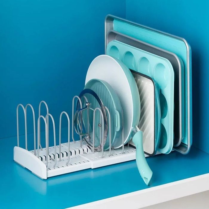 The expandable rack placed inside a cabinet, holding an assortment of pans and baking sheets.
