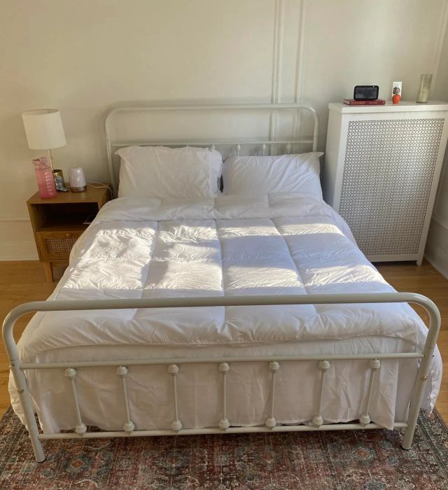 A neatly arranged bed with white linens, placed on a patterned rug in a clean, minimalist bedroom setting.