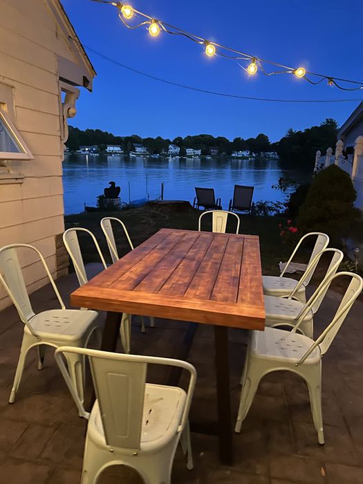 A reviewer's image of the outdoor dining table at night by the lake, surrounded by eight white chairs.