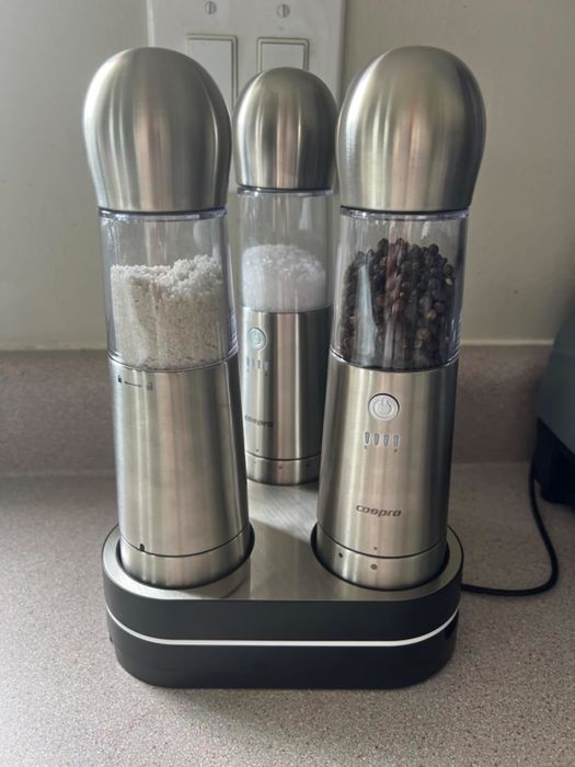 Electric salt and pepper grinders with a sleek metallic finish, placed on a countertop charging station