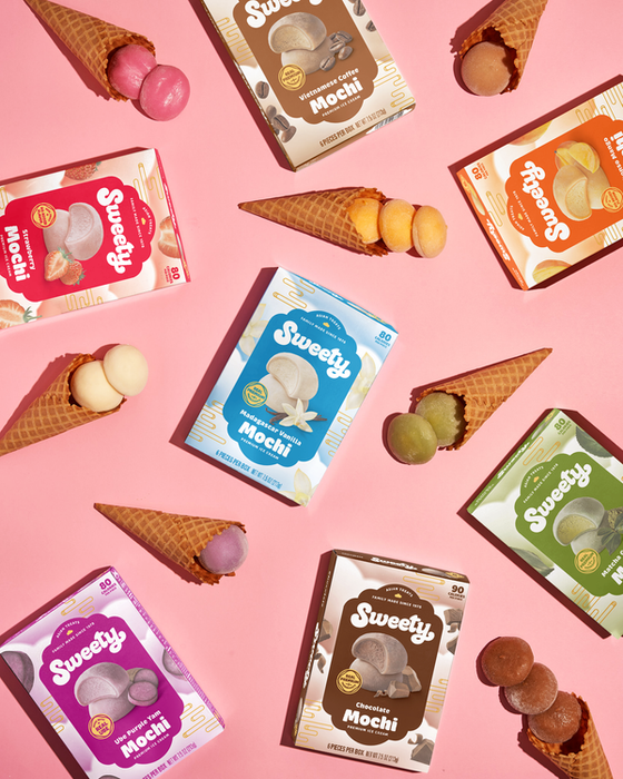 A variety of Sweety Mochi ice cream boxes in different flavors, surrounded by mochi balls placed in waffle cones
