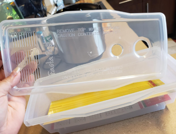 A hand holding the microwave pasta maker