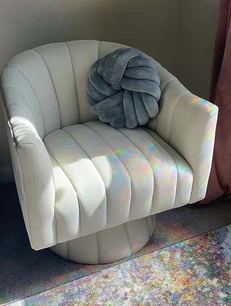 A chic white modern chair adorned with a gray decorative pillow, basking in soft natural sunlight.