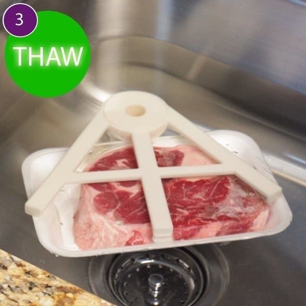 A piece of frozen meat in a tray is being thawed in a sink using a special plastic holder. The number 3 and the word 