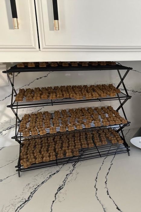 A three-tiered cooling rack filled with brown dog treats, placed next to a silver and black kitchen appliance on a marble countertop