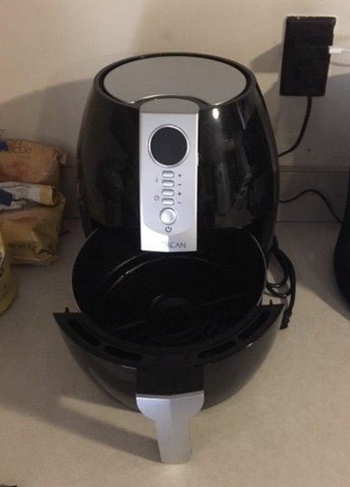 Air fryer appliance with various buttons for cooking settings and its bottom part open, revealing where food is placed before being slid back in to cook