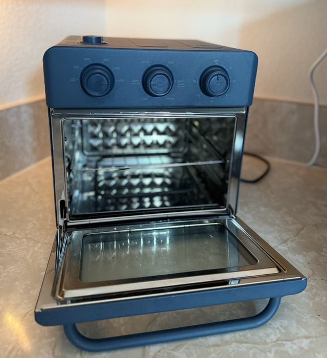 Electric toaster oven with an open door, stainless steel interior, and dial controls on a kitchen countertop