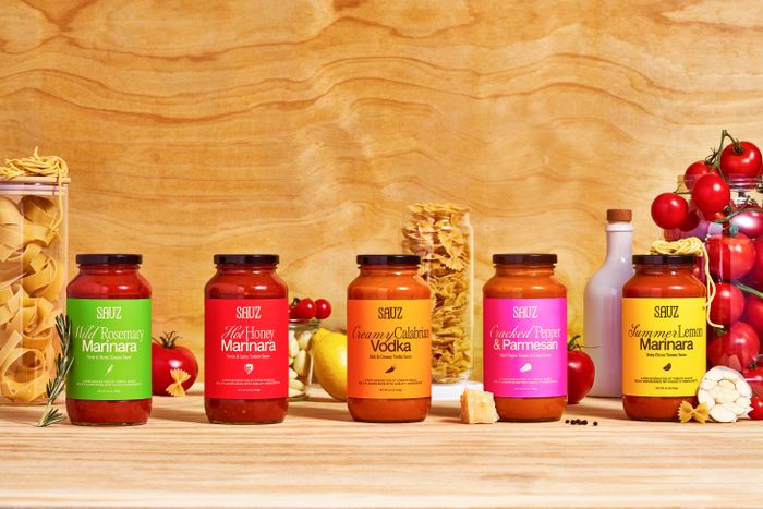 Five jars of SABUZ pasta sauce in various flavors are displayed on a kitchen counter, surrounded by pasta and fresh vegetables