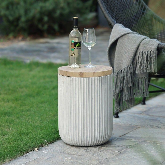 The cement side table with a bottle of wine and a full glass resting on top.