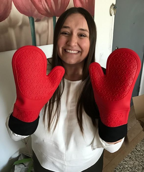 A person smiling while holding their hands up, wearing large red silicone oven mitts