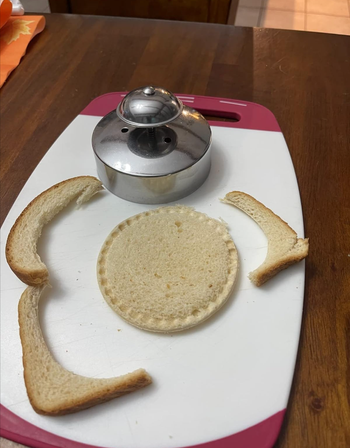 A round sandwich press placed on a cutting board with crusts removed, revealing a perfectly circular sandwich