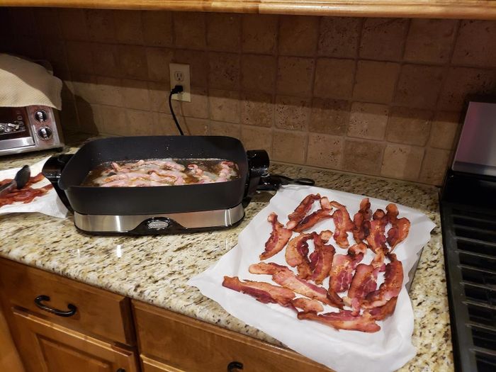 Bacon strips sizzling in a skillet, resting on paper towels on a kitchen counter