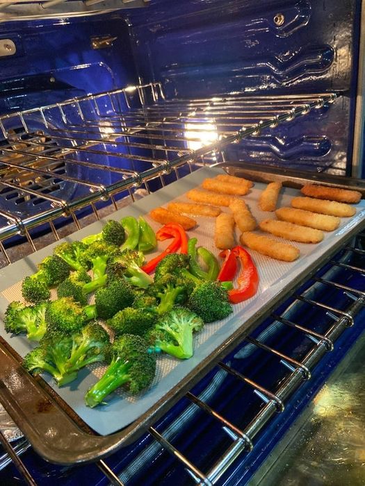 A reviewer's photo showing vegetable and mozzarella sticks cooking on a sheet pan, using the silicone baking mat.