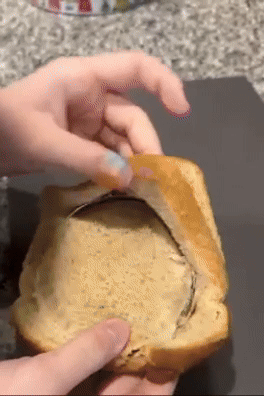 A person peeling off the top crust of a slice of brown bread, exposing a thin layer of filling inside