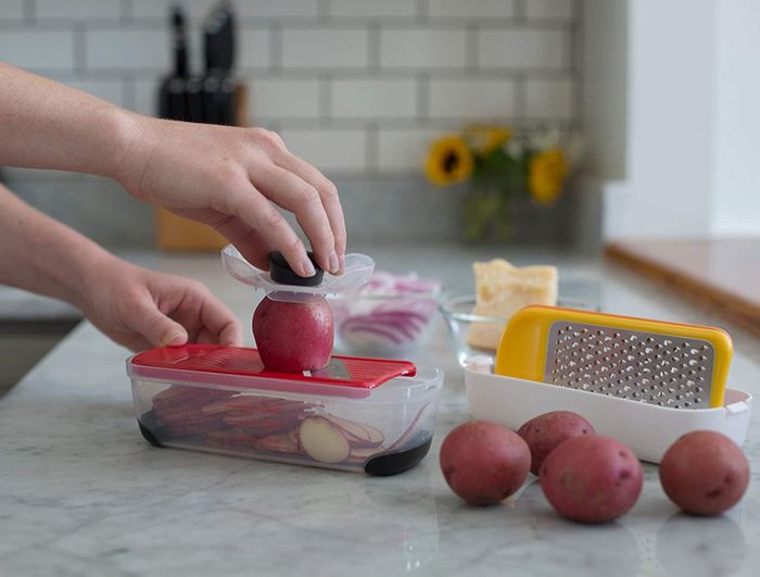 A person grating a red potato using the slicer plate