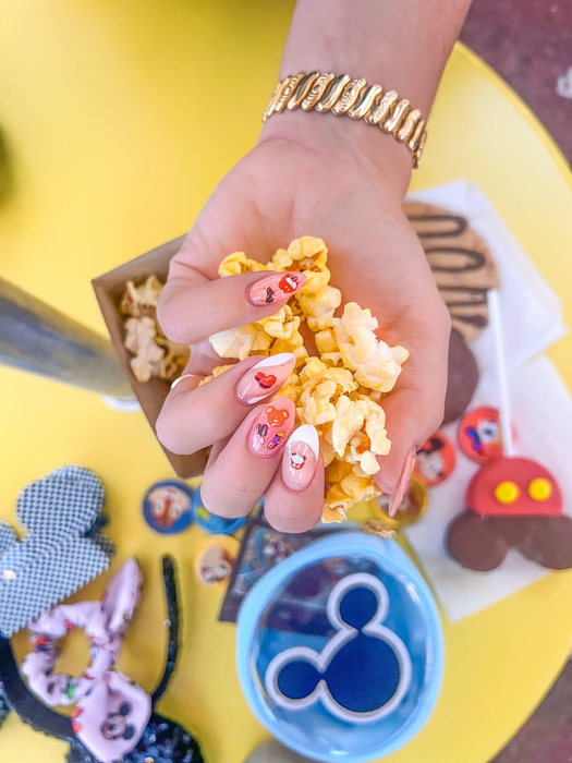 A hand holding popcorn with Disney snack nail art stickers adorning the nails