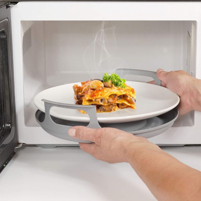 Hands placing a plate of lasagna onto a microwave rack inside a microwave