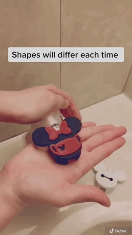 Person pressing on the Minnie-shaped soap dispenser attachment to create Mickey Mouse-shaped suds