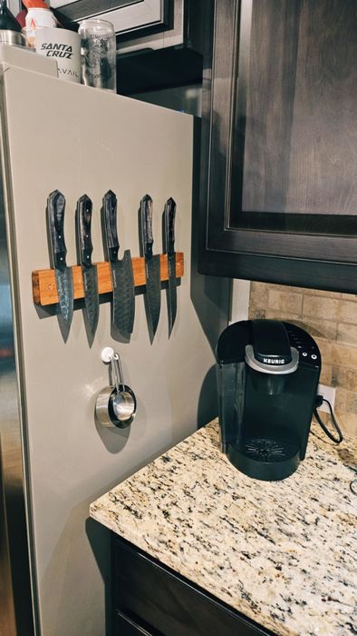 A kitchen countertop with a Keurig coffee maker and a magnetic knife holder displaying five kitchen knives on the side of a fridge