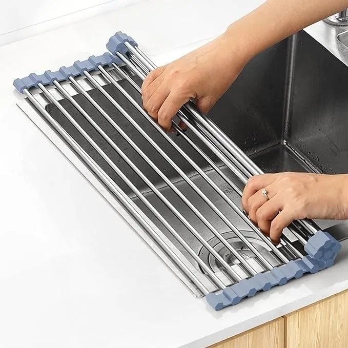 Hands setting up a stainless steel roll-up dish drying rack over a kitchen sink